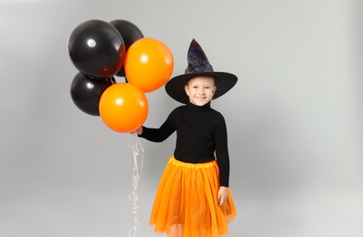 Cute little girl with balloons wearing Halloween costume on grey background