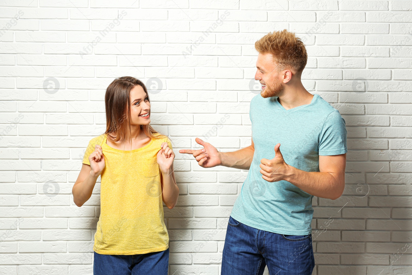 Photo of Young couple wearing blank t-shirts near white brick wall. Mockup for design