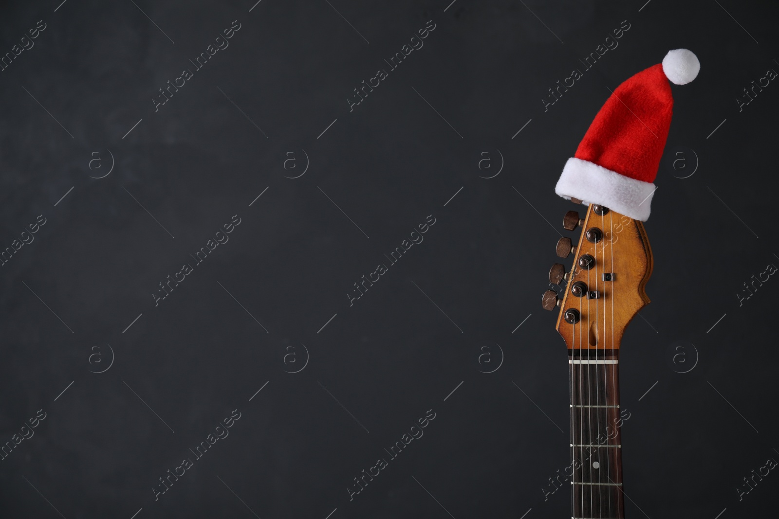 Photo of Guitar with Santa hat on dark background, space for text. Christmas music