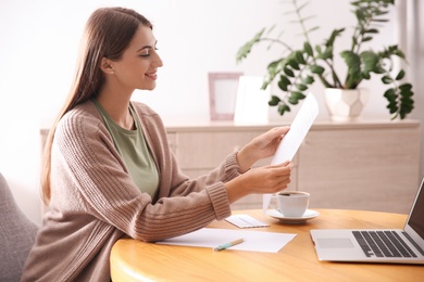 Woman reading letter at wooden table in room