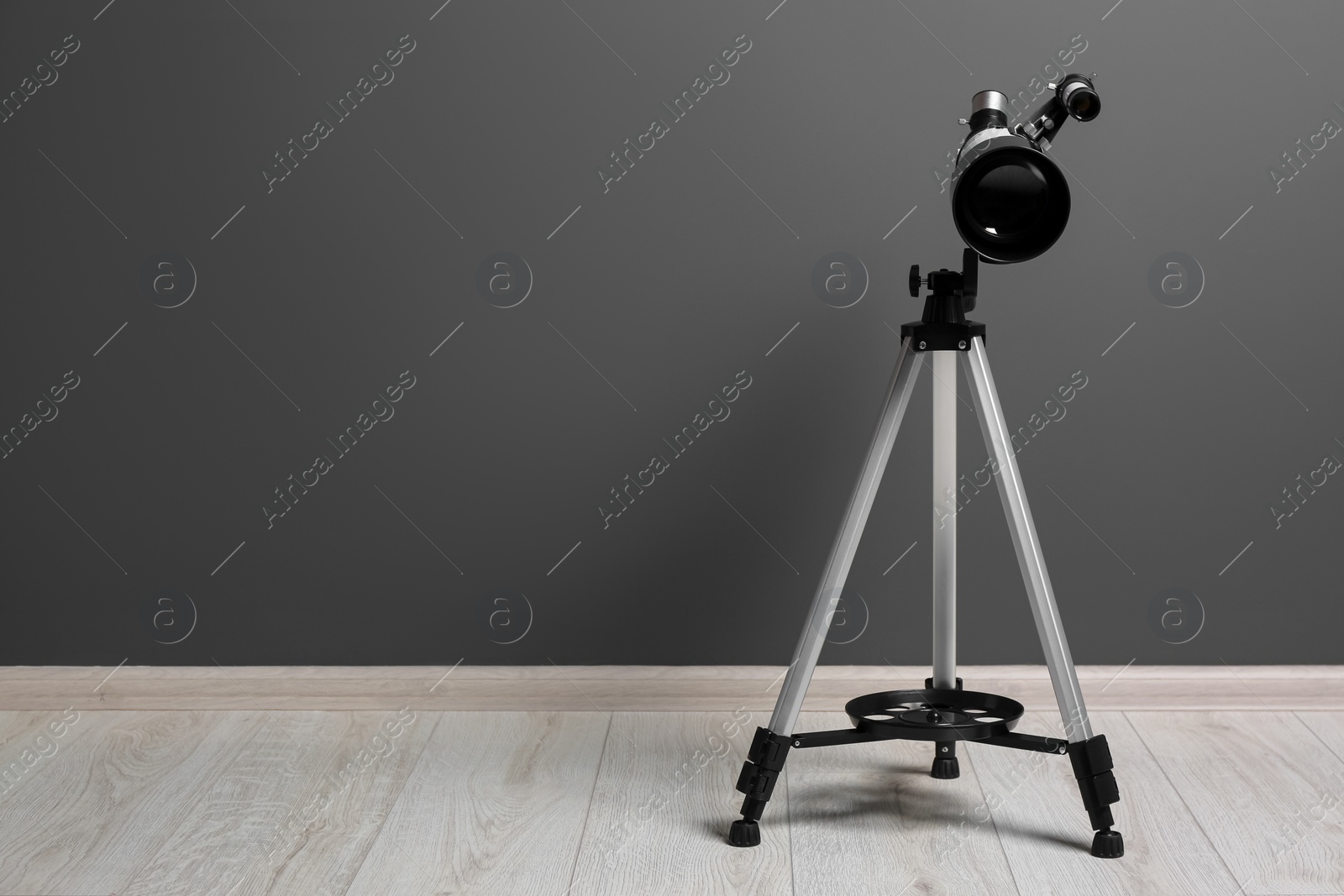 Photo of Tripod with modern telescope near grey wall. Space for text