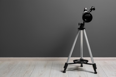 Tripod with modern telescope near grey wall. Space for text