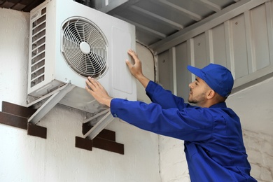 Photo of Professional technician maintaining modern air conditioner outdoors