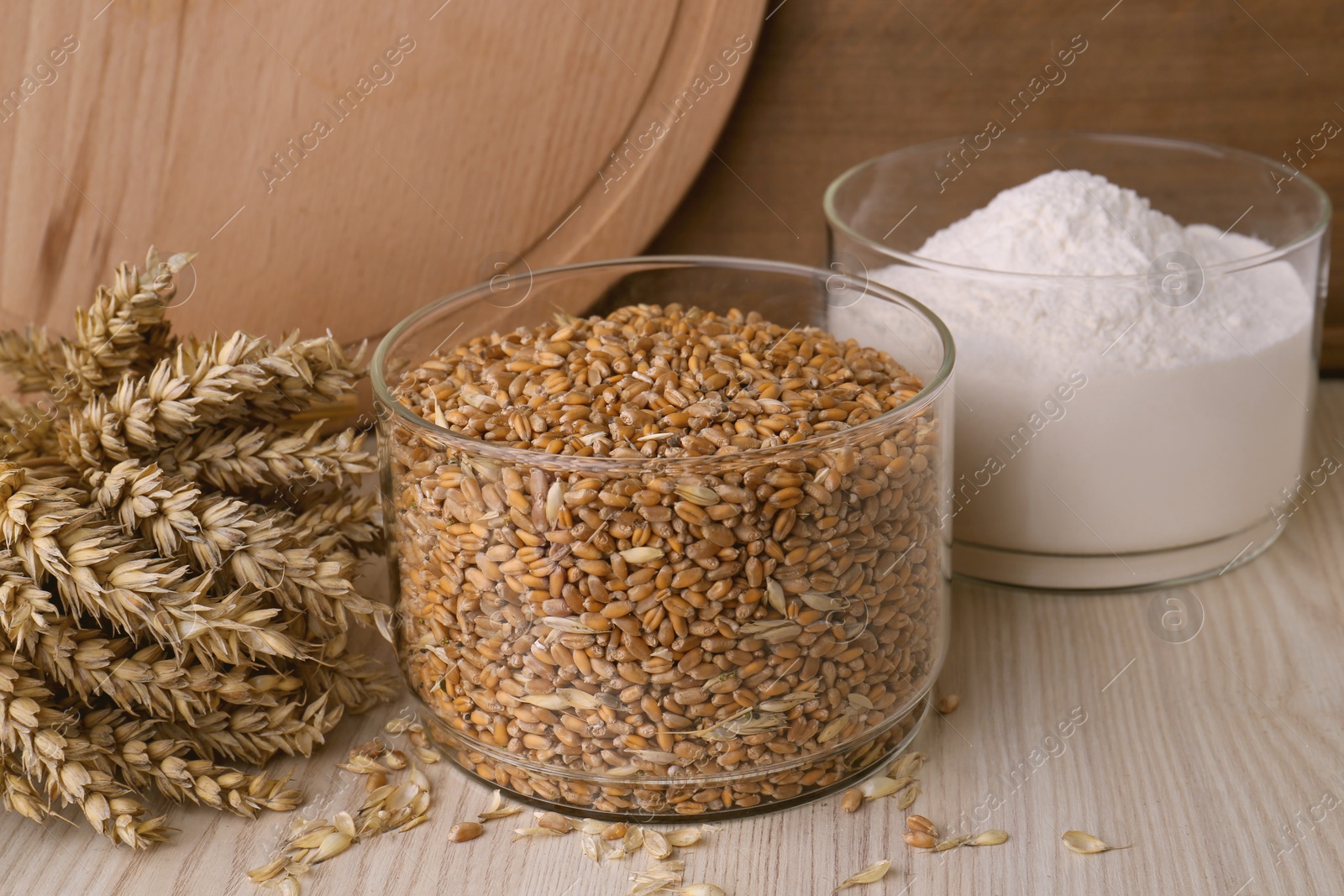 Photo of Wheat grains in bowl, spikes and flour on wooden table