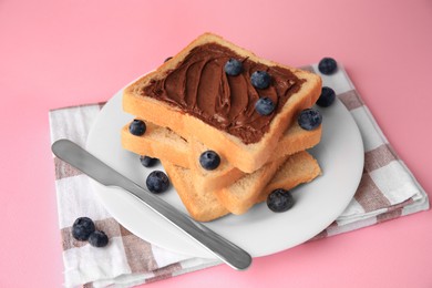 Photo of Tasty toast with chocolate paste and blueberries on pink table