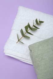 Photo of Different soft towels and eucalyptus branch on violet background, top view