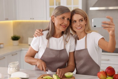 Photo of Happy daughter taking selfie with her mature mother while cooking together in kitchen