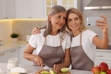 Happy daughter taking selfie with her mature mother while cooking together in kitchen