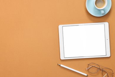 Photo of Modern tablet, glasses, stylus and cup of coffee on orange background, flat lay. Space for text