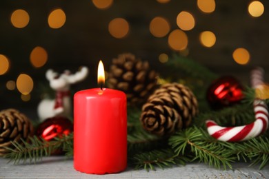 Photo of Burning candle and Christmas decor on wooden table against blurred festive lights, space for text 