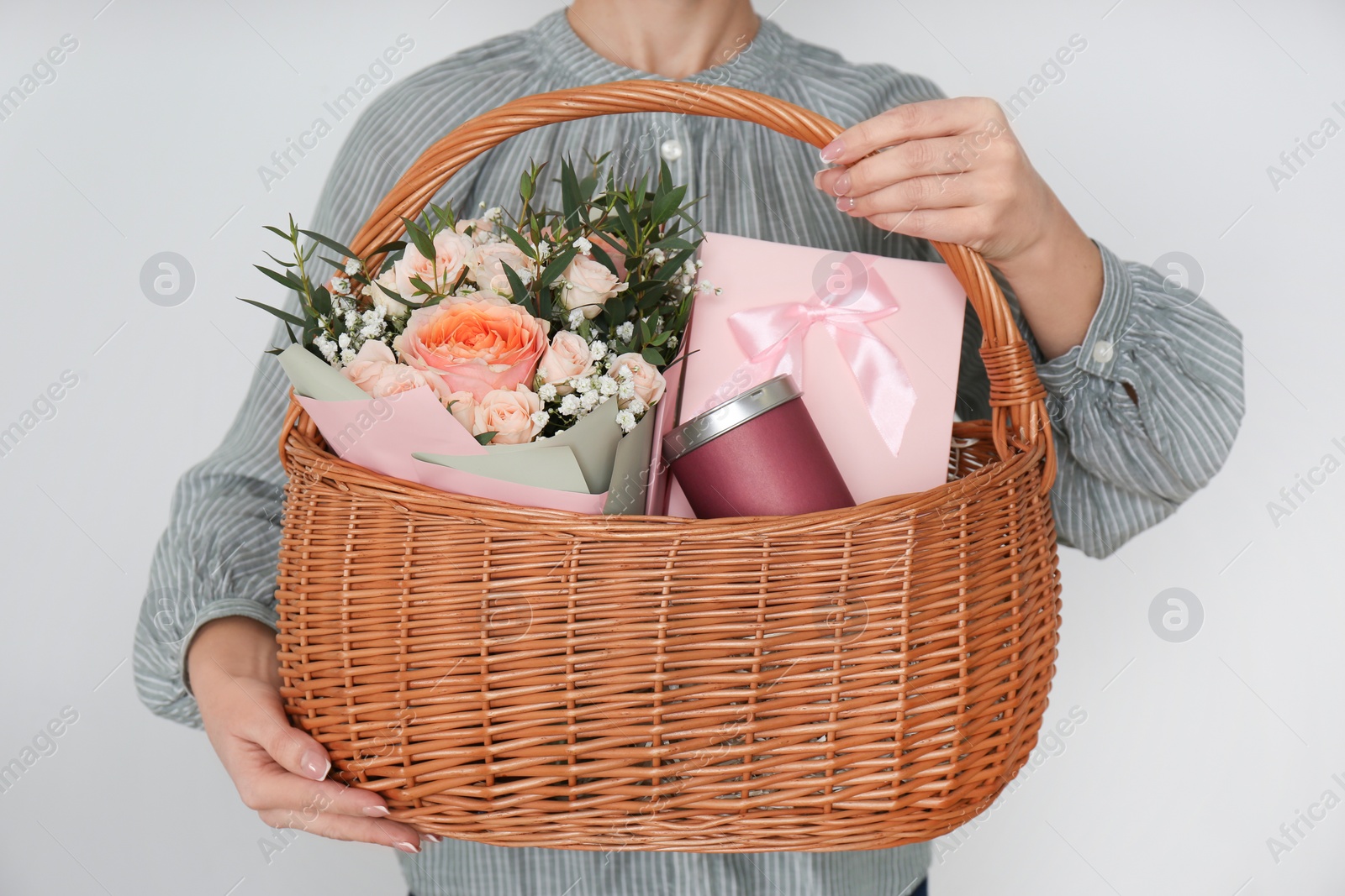 Photo of Woman holding wicker basket with different gifts on grey background, closeup