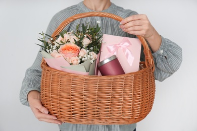 Woman holding wicker basket with different gifts on grey background, closeup