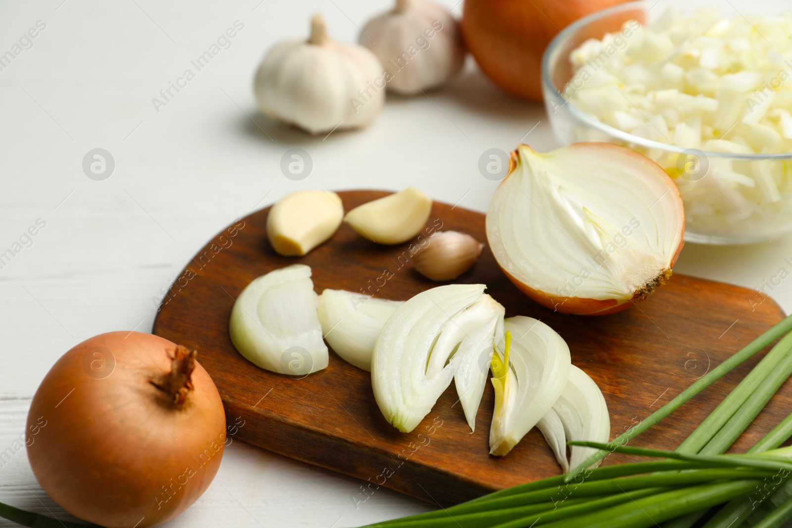 Photo of Board with cut onion and garlic on white wooden table