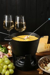 Photo of Fondue pot with melted cheese, glasses of wine, forks and different products on wooden table