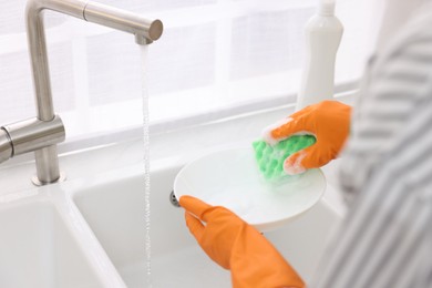 Woman washing plate above sink in modern kitchen, closeup