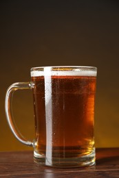 Photo of Mug with fresh beer on wooden table against dark background