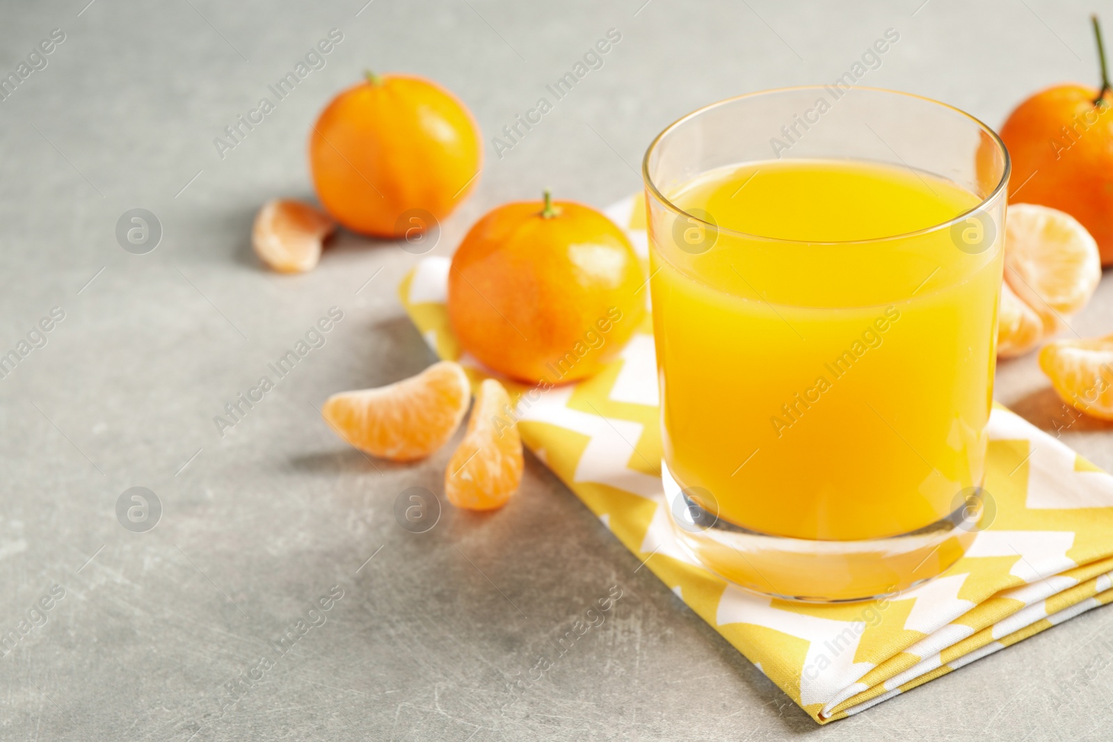 Photo of Glass of fresh tangerine juice and fruits on light grey table. Space for text