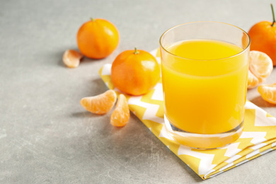 Photo of Glass of fresh tangerine juice and fruits on light grey table. Space for text