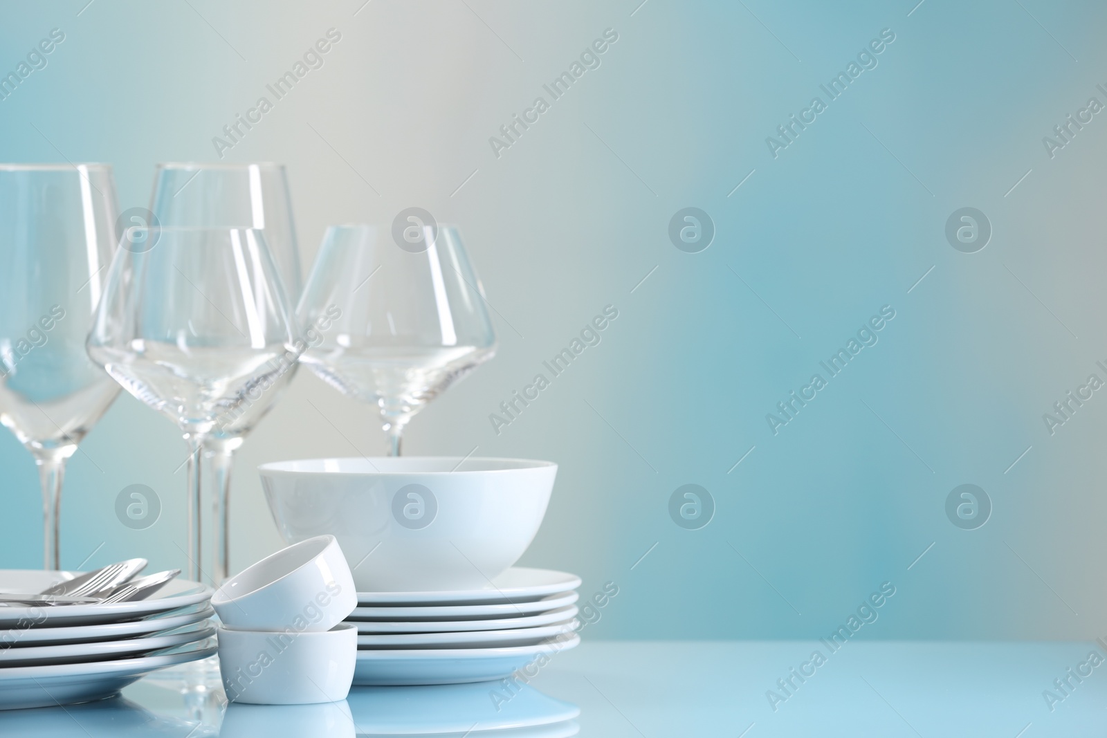 Photo of Set of many clean dishware, cutlery and glasses on light blue table. Space for text