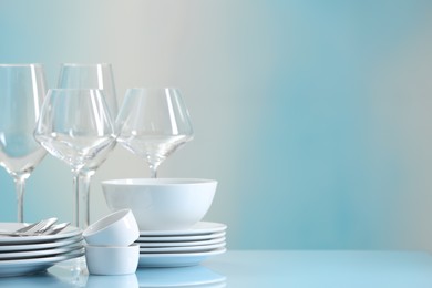 Photo of Set of many clean dishware, cutlery and glasses on light blue table. Space for text