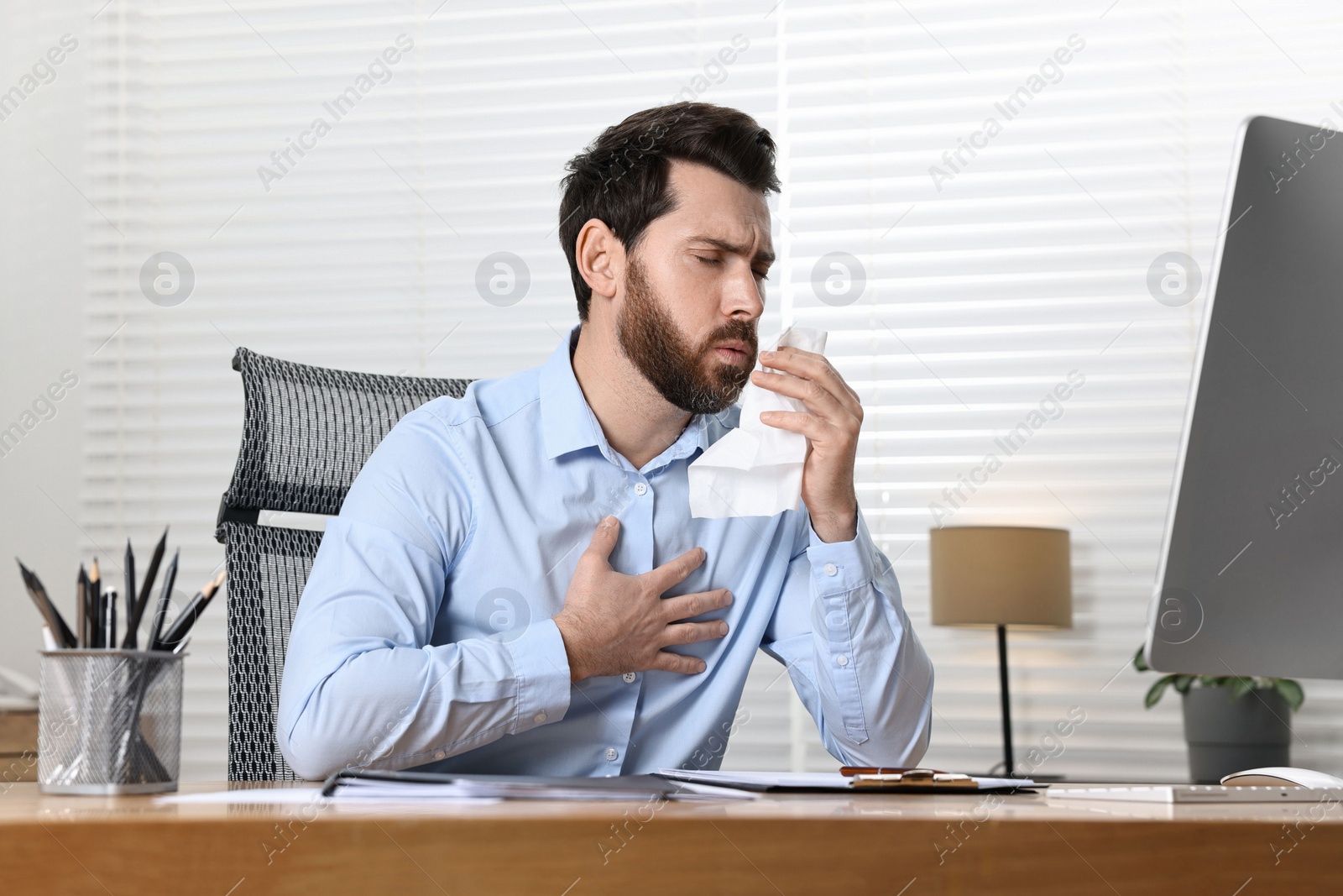 Photo of Sick man with tissue coughing at workplace in office