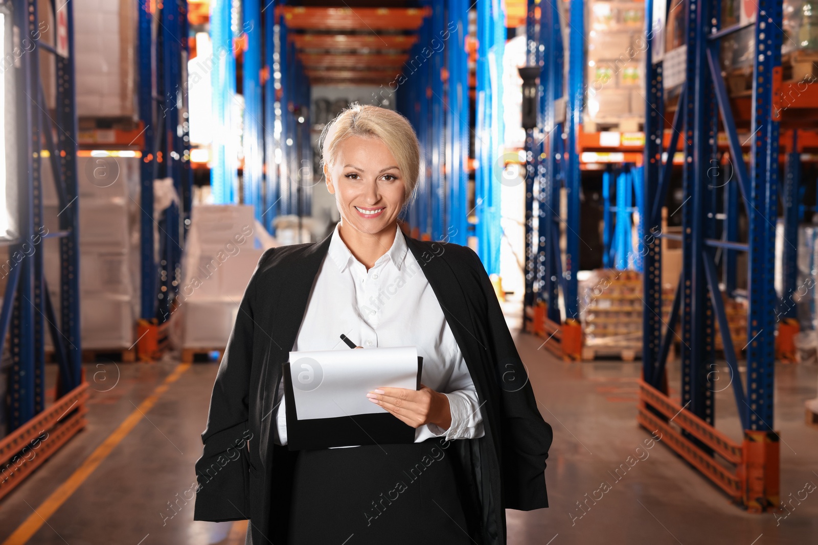 Photo of Happy manager holding clipboard in warehouse with lots of products