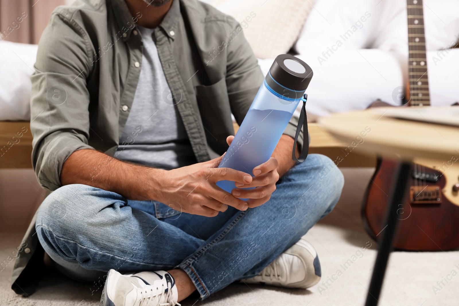Photo of Man with transparent plastic bottle of water sitting on floor indoors, closeup