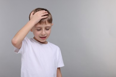 Little boy suffering from headache on grey background, space for text
