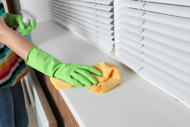 Photo of Woman cleaning window sill with rag, closeup