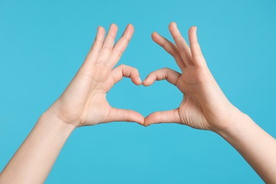 Photo of Young woman making heart with her hands on color background, closeup
