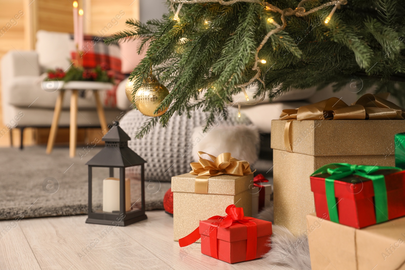 Photo of Gift boxes under Christmas tree and lantern with candle indoors