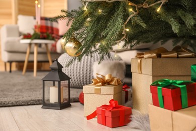 Gift boxes under Christmas tree and lantern with candle indoors