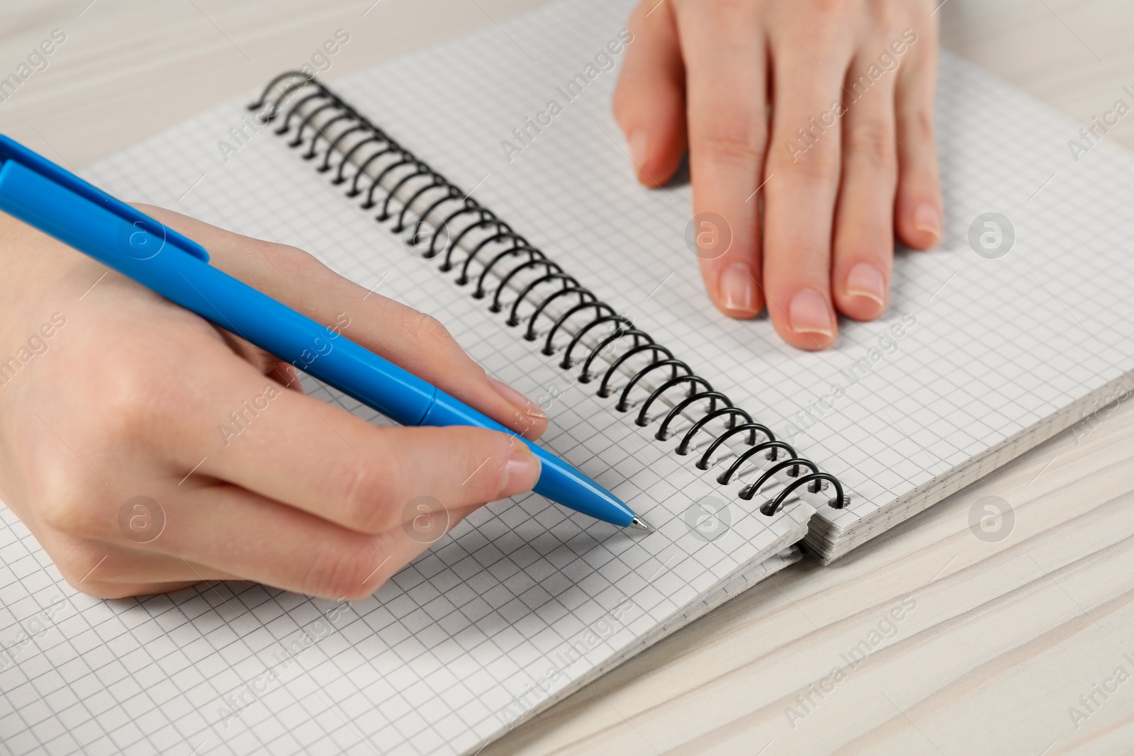 Photo of Woman writing in notebook at white wooden table, closeup