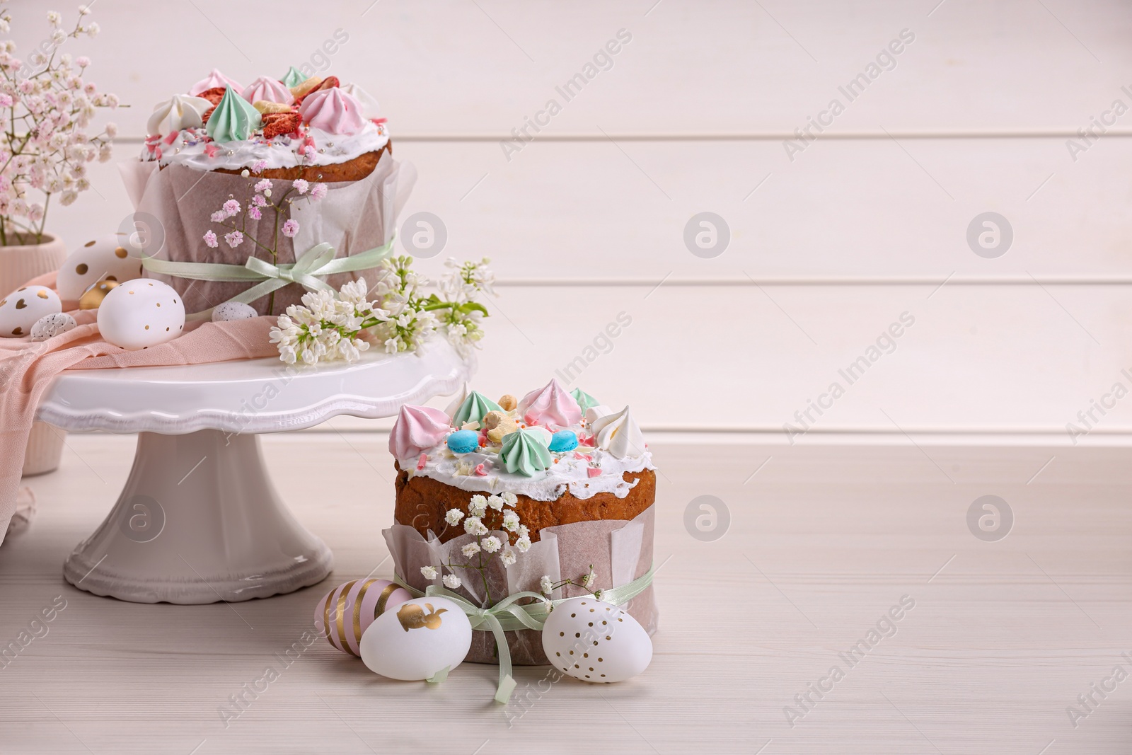 Photo of Traditional Easter cakes with meringues and painted eggs on white wooden table, space for text