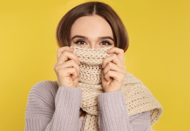 Beautiful young woman in scarf and sweater on yellow background. Winter season