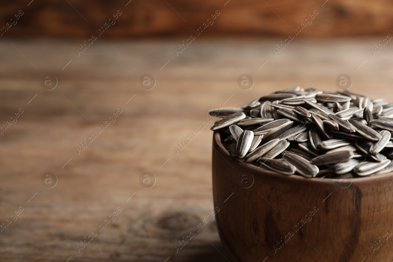 Photo of Raw sunflower seeds in bowl on wooden table, closeup. Space for text