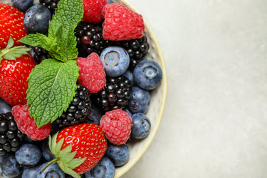 Photo of Mix of different fresh berries and mint in bowl on light grey table, top view. Space for text