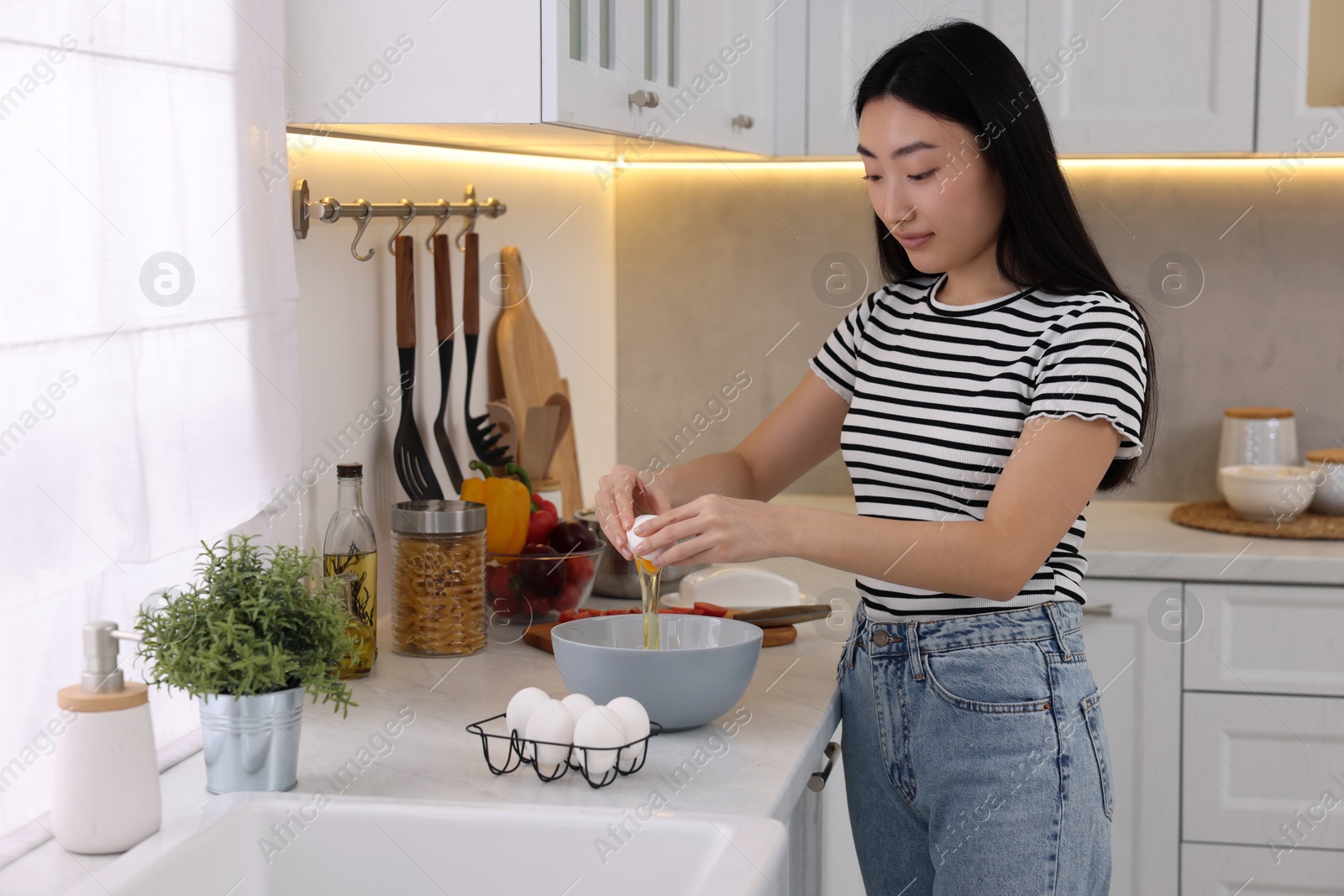 Photo of Cooking process. Beautiful woman breaking egg into bowl in kitchen