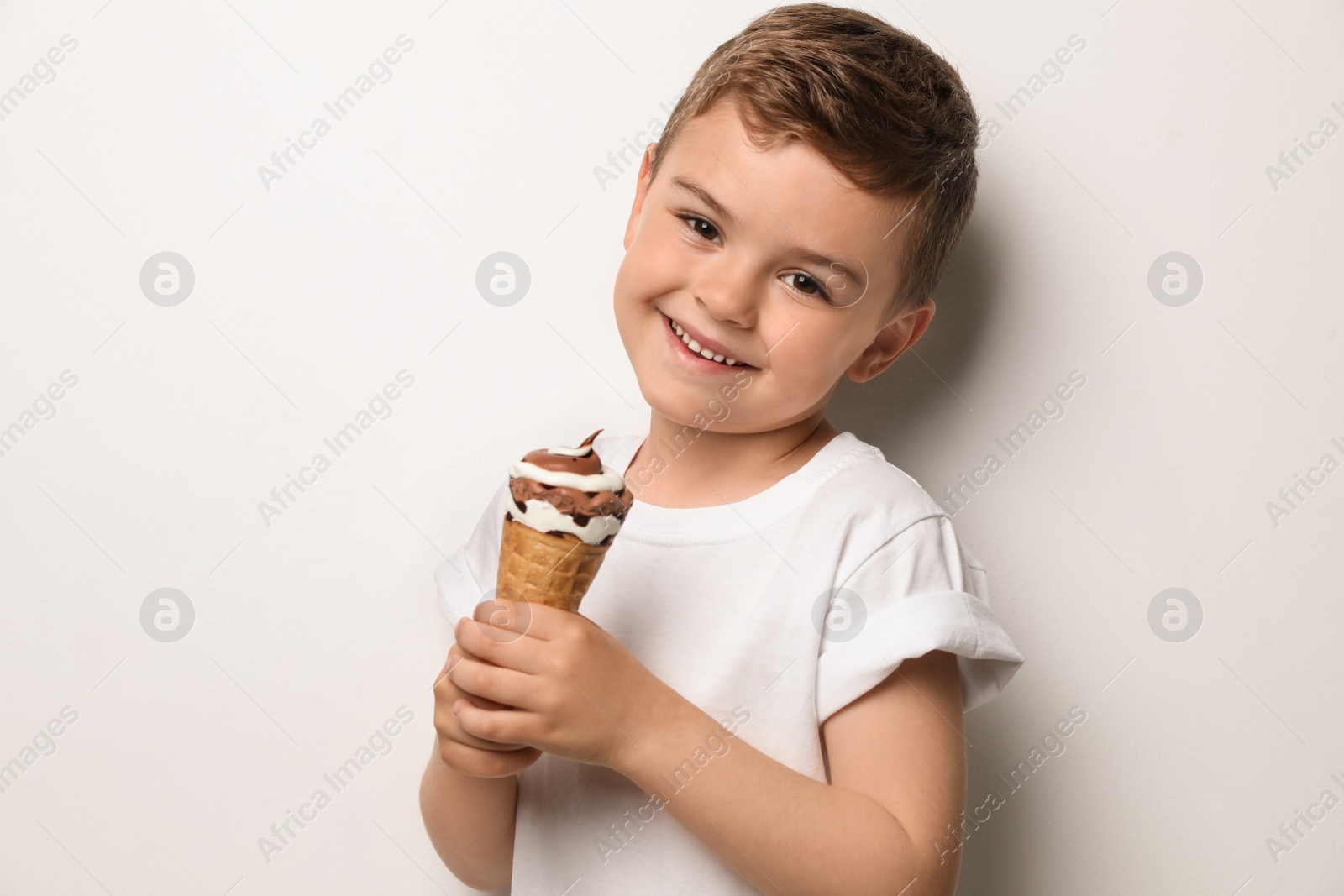 Photo of Adorable little boy with delicious ice cream against light background