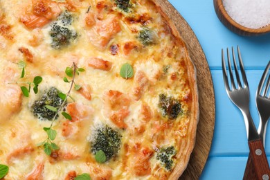 Photo of Delicious homemade salmon quiche with broccoli, forks and salt on light blue wooden table, flat lay