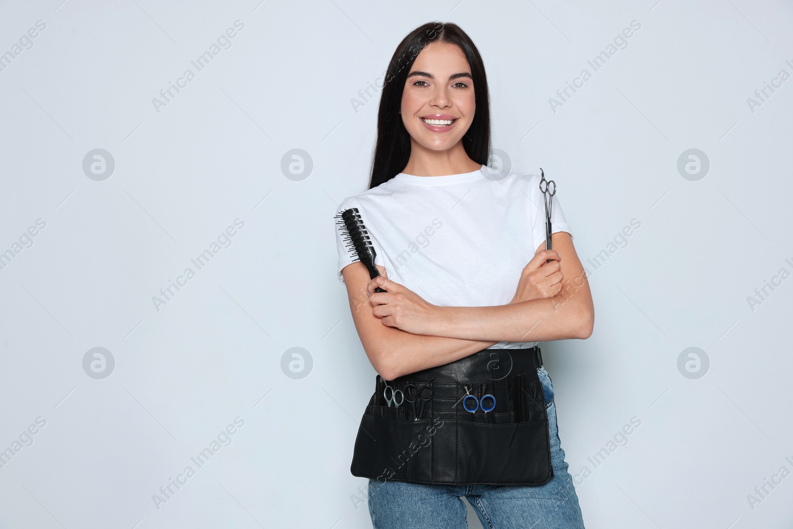 Photo of Portrait of happy hairdresser with professional scissors and vent brush on light background, space for text