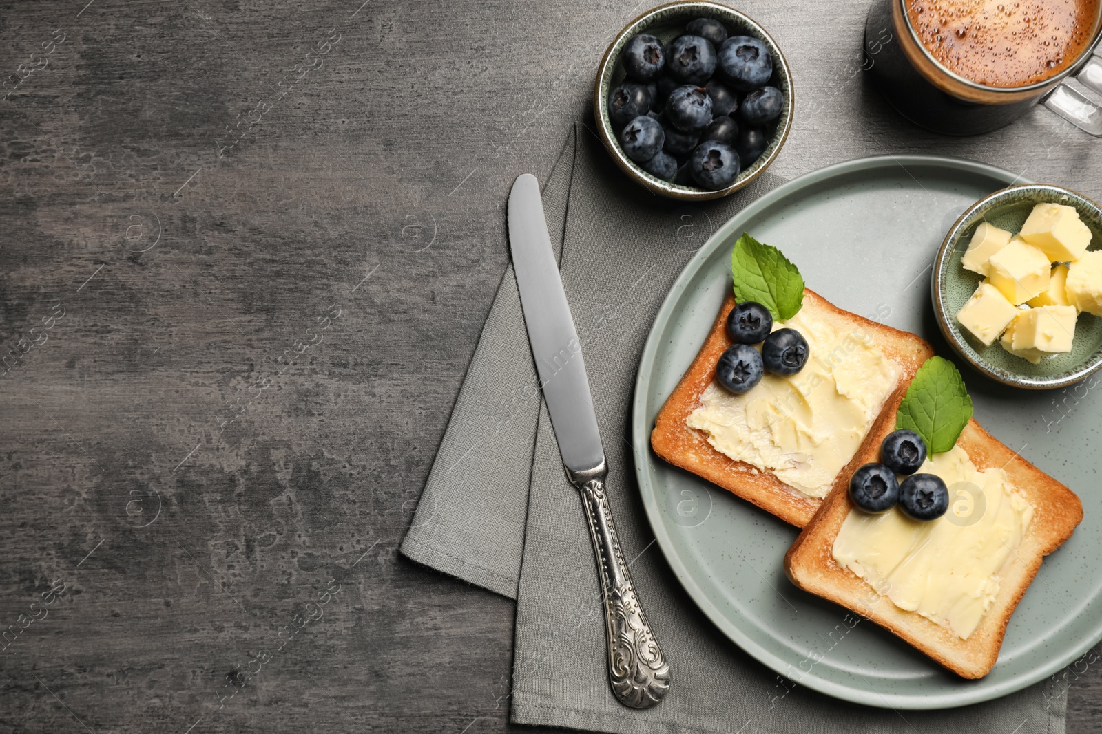Photo of Delicious toasts served with butter, blueberries and coffee on grey wooden table, flat lay. Space for text