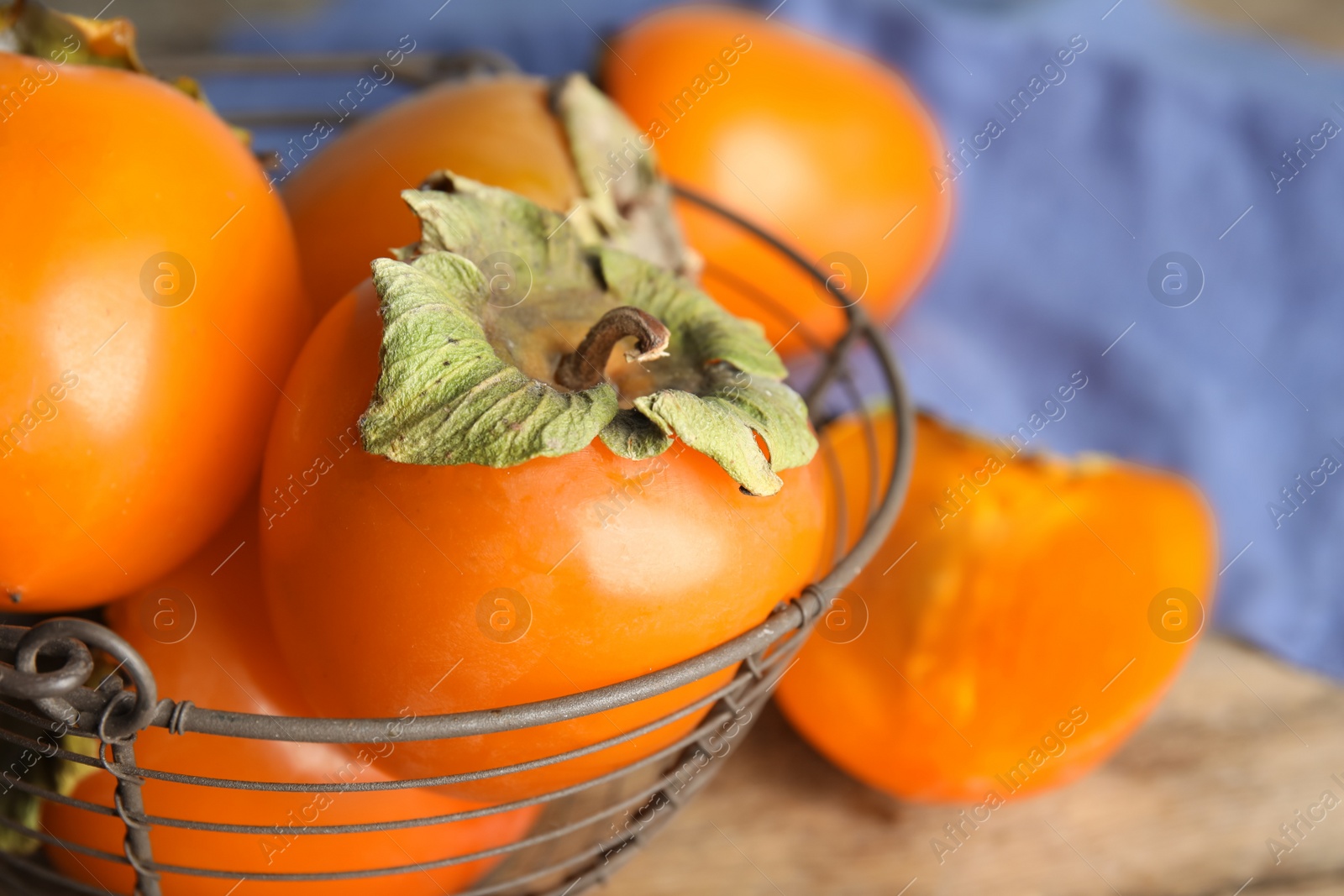 Photo of Delicious fresh persimmons in metal basket on table, closeup