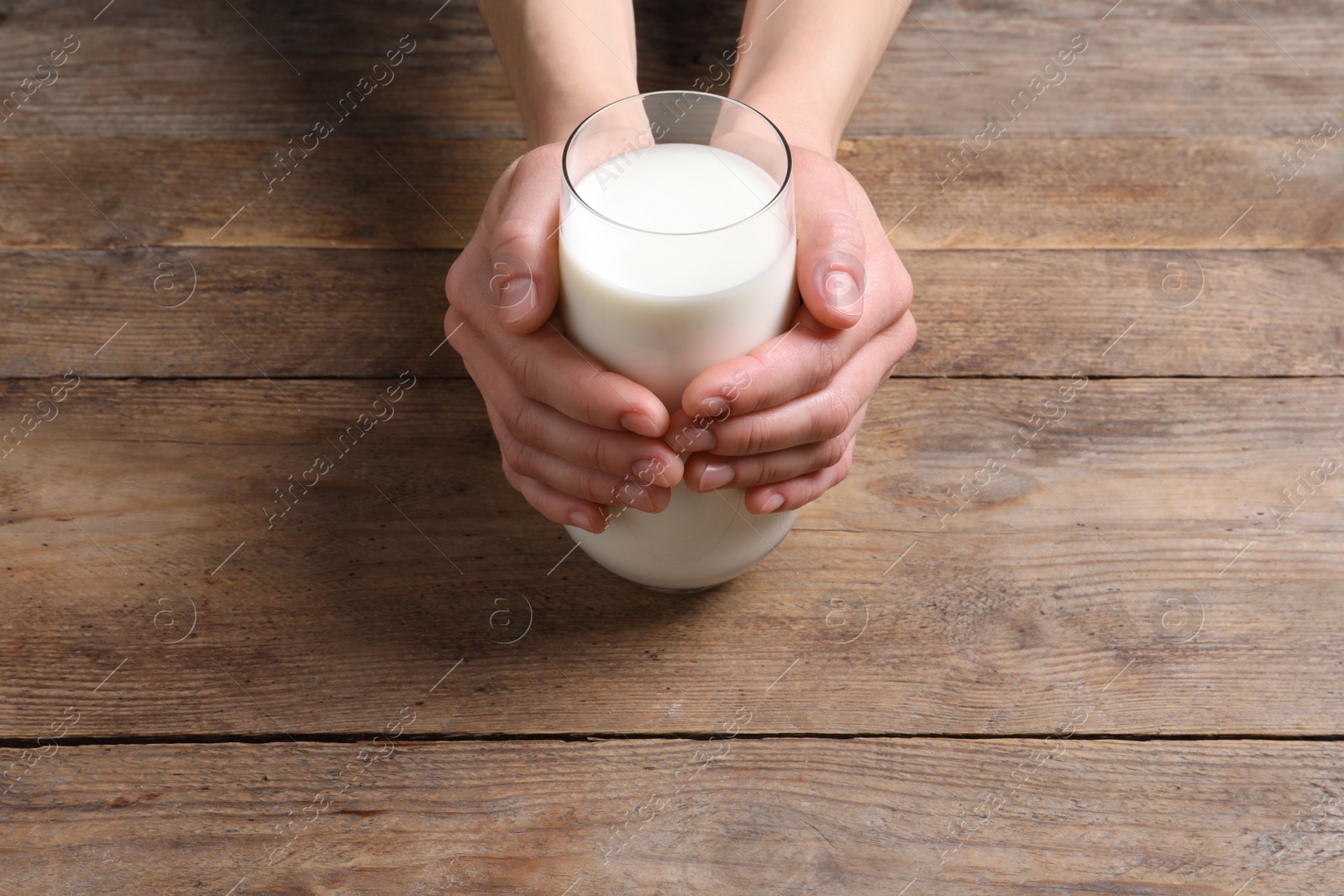 Photo of Woman holding glass of milk at wooden table, closeup