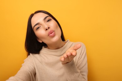Photo of Beautiful young woman taking selfie while blowing kiss on orange background. Space for text