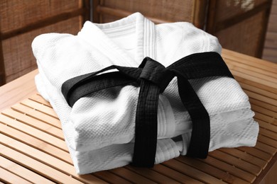 Photo of Martial arts uniform with black belt on table indoors