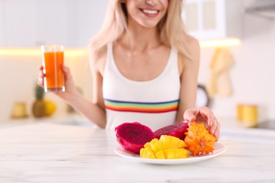 Woman with fresh juice and exotic fruits at table in kitchen, closeup