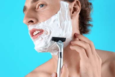 Handsome young man shaving on color background