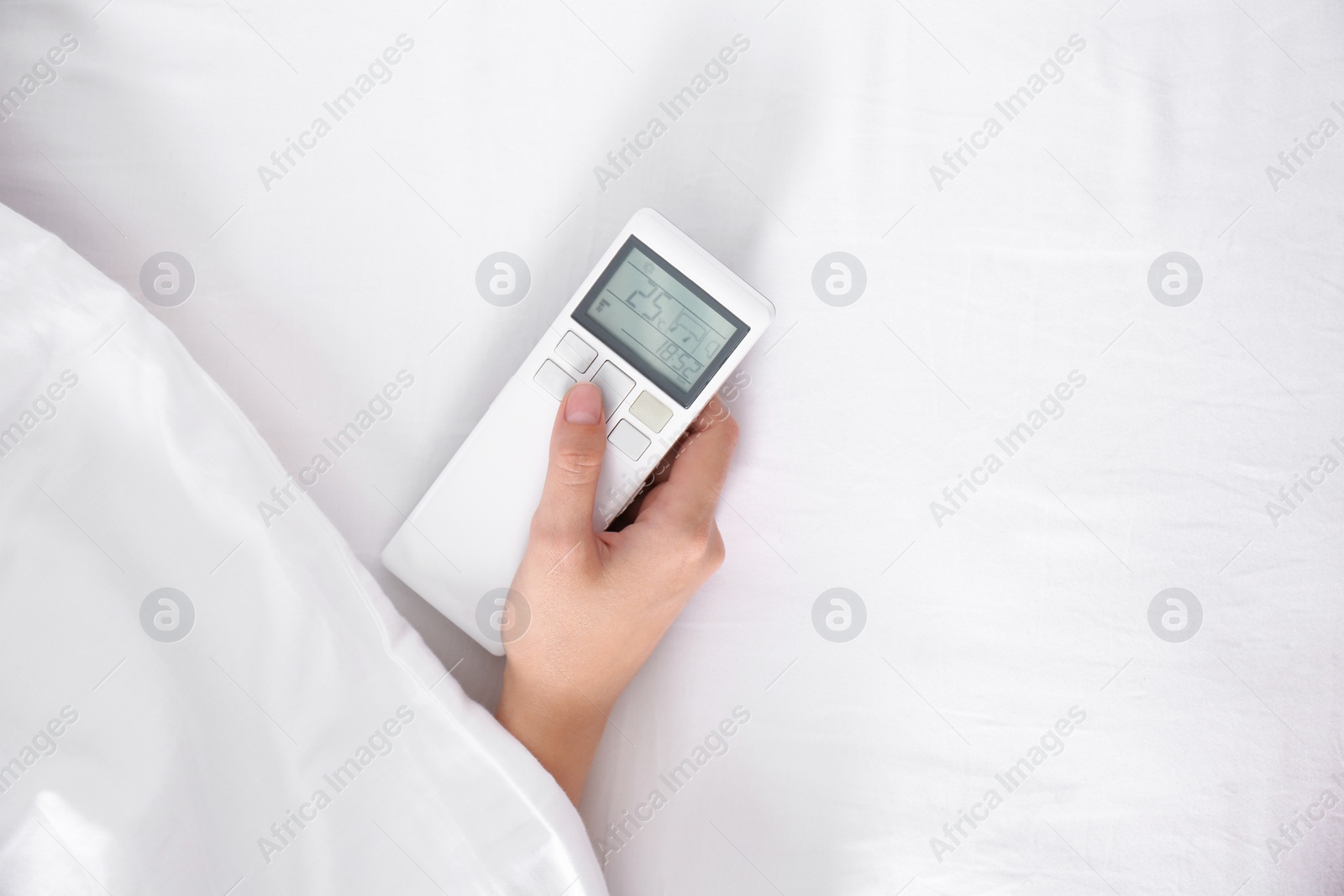 Photo of Woman holding air conditioner remote control in bed, focus on hand