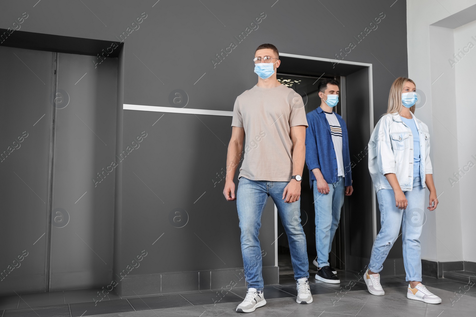 Photo of Group of people in face masks walking out from elevator. Protective measure